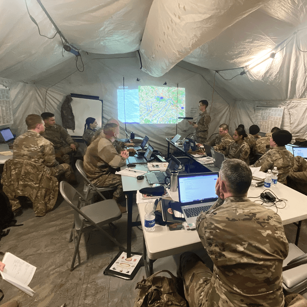soldiers sitting around a table with laptops, having a presentation